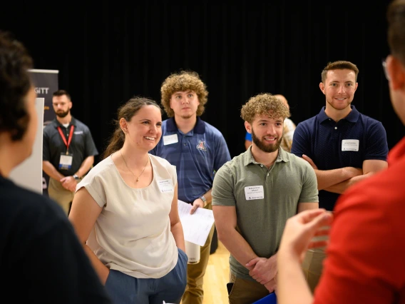A group of students stands listening to another student speak