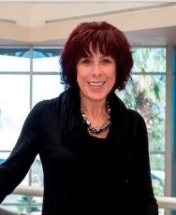 Sharon ONeal An image of Sharon ONeal in a black outfit standing in front of windows