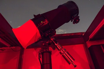 Team 16065 telescope Photo of a telescope pointing at the night sky out of an opening in a roof with a red light on inside