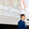 A young man with brown hair and a brown mustache reads a speech.