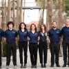 Seven students with blue shirts pose for a photo in front of palm trees.